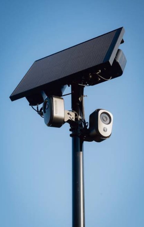 A solar-powered license plate reader with two cameras mounted on a pole against a clear blue sky